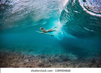 woman in bikini doing duck dive with the surfboard under the waves