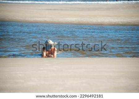 Woman in a bikini and hat lying in the waters of the sea. Taquari, Guaibim beach, Valenca, Bahia.