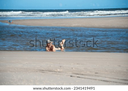 Woman in a bikini and hat lying in the waters of the sea raising her feet. Taquari, Guaibim beach, Valenca, Bahia.
