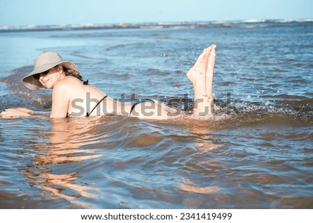 Woman in bikini and hat relaxing and playing by the sea. Taquari, Guaibim beach, Valenca, Bahia.