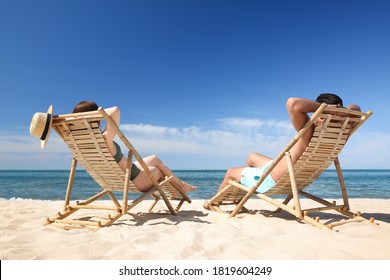 Woman in bikini and her boyfriend on deck chairs at beach. Lovely couple - Powered by Shutterstock