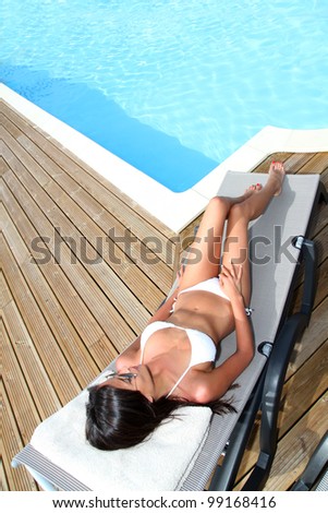 Woman in bikini relaxing in deck chair by pool
