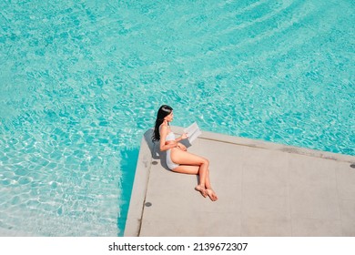 Woman In Bikini Sitting On The Edge Of Swimming Pool, Top View. Summer Vacation, Tanning And Leisure Concept