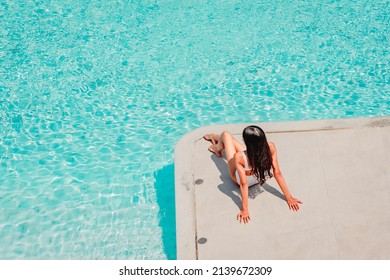 Woman In Bikini Sitting On The Edge Of Swimming Pool, Top View. Summer Vacation, Tanning And Leisure Concept