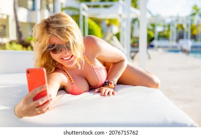 Woman in bikini taking selfie photo while sunbathing on vacation in luxury tropical resort
