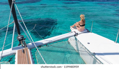 Woman in bikini tanning and relaxing on a summer sailin cruise, sitting on a luxury catamaran in picture perfect turquoise blue lagoon near Spargi island in Maddalena Archipelago, Sardinia, Italy.