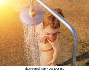 A woman in a bikini is washing herself under a shower outdoors on a sunny day. Beach shower - Powered by Shutterstock