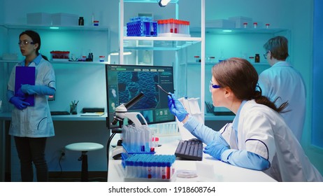 Woman Biochemist Checking Manifestations Of Virus Working On Computer In Equipped Lab Late At Night. Team Of Doctors Examining Vaccine Evolution Using High Tech Researching Diagnosis Against Covid19