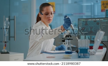 Woman biologist using micro pipette with test tube and beaker for experiment in science laboratory. Biochemistry specialist working with lab equipment and glassware for development.