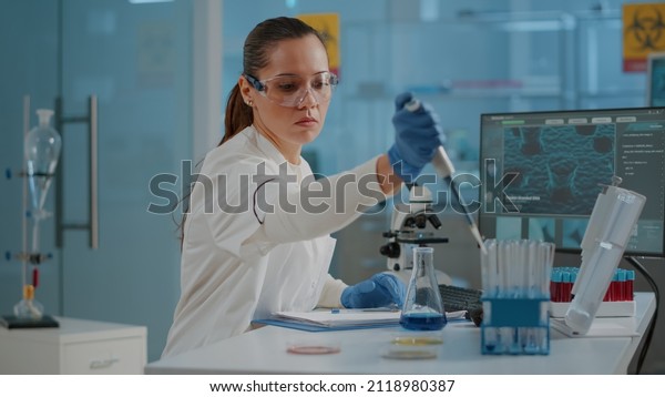 Woman\
biologist using micro pipette with test tube and beaker for\
experiment in science laboratory. Biochemistry specialist working\
with lab equipment and glassware for\
development.