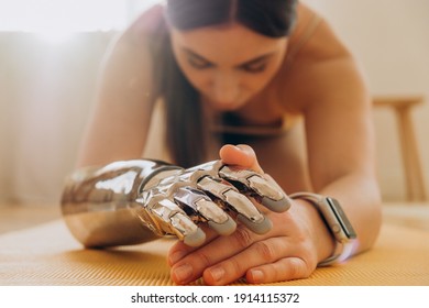 Woman with bionic prosthetic arm does yoga at home on a mat on a sunny day with a modern fitness watch, hands close up