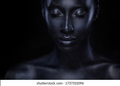 Woman with black body paint. Cheerful young african girl with bodypaint. An amazing model with art makeup. Closeup face.