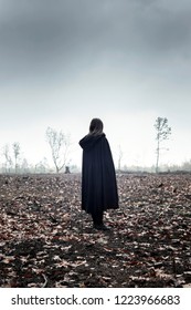 Woman In Black Cape In Moody Countryside.