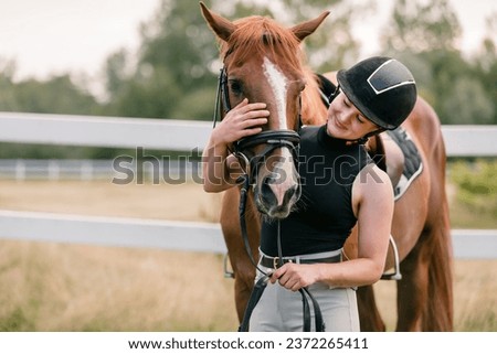 Woman with a black helmet stroking a beautiful chestnut horse head, close up shot. Human and animal relation concept.