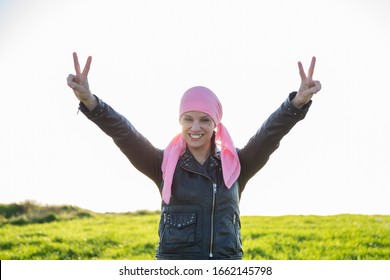 Woman in a black jacket with a pink headscarf in a field. With her arms raised in the form of victory and celebration. Concept of breast cancer. - Shutterstock ID 1662145798
