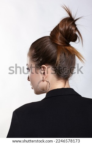 Woman in a black jacketposing on gray background. Female with long brown hair  tied in a knot at the top of the head. Back view Stock photo © 