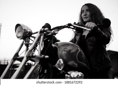 Woman In A Black Leather Jacket Sits On A Motorcycle. Portrait Of A Serious Girl Driving A Bike.