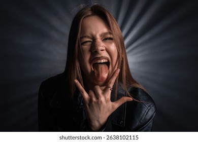 A woman in a black leather jacket sticks out her tongue and makes a hand gesture, conveying energy and excitement against a dark backdrop. For fashion editorials, clothing brands, or accessory ads.