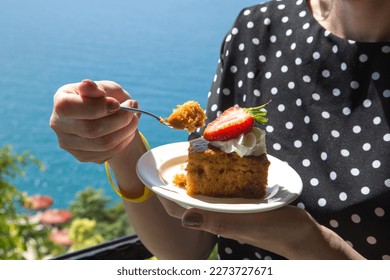 A woman in black polka dot dress tastes piece of cake with cream and strawberries. - Powered by Shutterstock