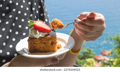 A woman in a black polka dot dress tastes a piece cake with cream and strawberries. - Powered by Shutterstock