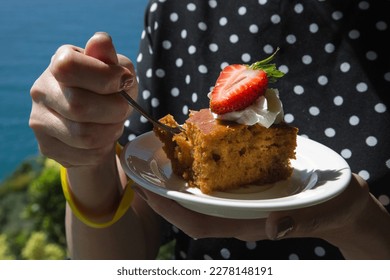 A woman black polka dot dress tastes a piece of cake with cream and strawberries. - Powered by Shutterstock