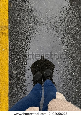 Woman in black rain boot shoes and blue jeans standing on gray street highway. Photo taken while walking after the rain. street photography, lifestyle. yellow line on the road.