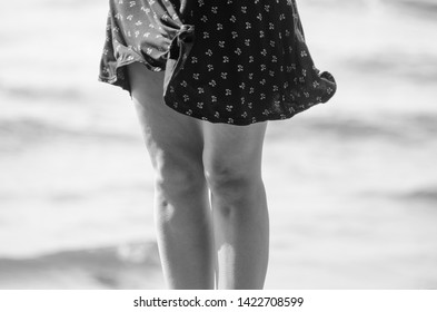 Woman In Black Skirt In The Windy Weather On Beach. Goosebumps On Legs Skin. Black And White Processing