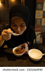 A Woman In A Black Veil Eats Delicious Tom Yum Soup At An Indonesian Restaurant.