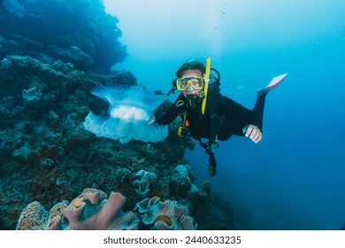 A woman in a black wetsuit is swimming in the ocean and pointing at a jellyfish in the great barrier reef - Powered by Shutterstock