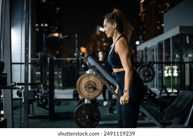 A woman in black workout clothes performs a cable row exercise at an outdoor gym at night. - Powered by Shutterstock