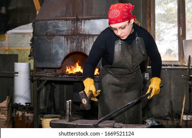 woman blacksmith metal artist forge a hot metal workpiece with hammer on the anvil in a traditional workshop - Powered by Shutterstock