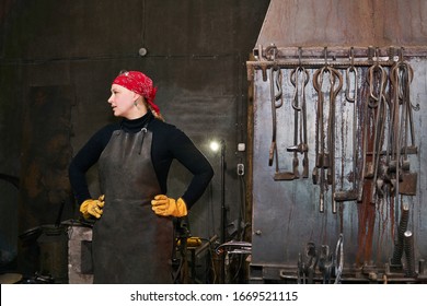 woman blacksmith metal artist in her workshop next to a forge furnace and tools - Powered by Shutterstock