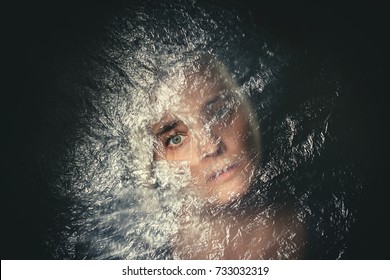 Woman with blank, terrified expression peeking through hole in plastic curtain, scared in dark - Powered by Shutterstock