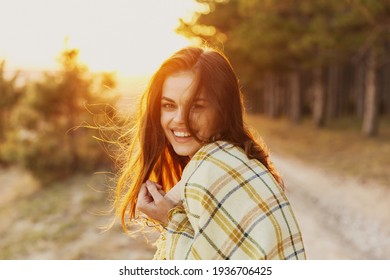 woman with a blanket on her shoulders laughs the sunset in the background and conifers on the side - Powered by Shutterstock