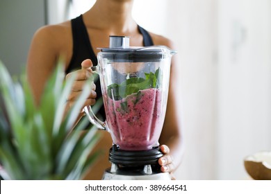 Woman blending spinach, berries, bananas and almond milk to make a healthy green smoothie - Shutterstock ID 389664541