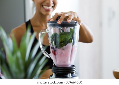 Woman blending spinach, berries, bananas and almond milk to make a healthy green smoothie