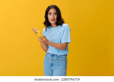 Woman blogger with a phone in her hands in a blue t-shirt and jeans on a yellow background smile signs gestures symbols, online communication and video call, copy space, free background - Shutterstock ID 2280796719