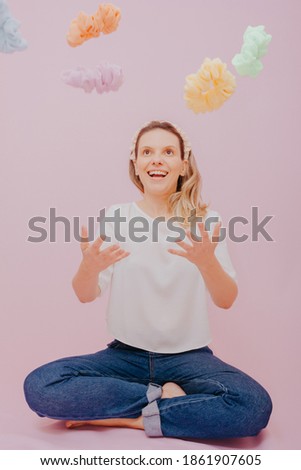 
Woman with blond hair. Studio portrait of woman tossing hair ties upwards. Pink Background.