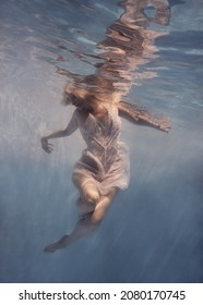     A woman with blond hair in a white dress swims underwater as if flying in zero gravity                           