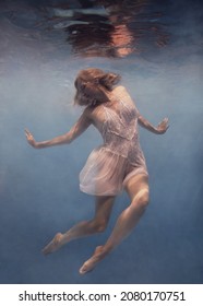     A Woman With Blond Hair In A White Dress Swims Underwater As If Flying In Zero Gravity                           