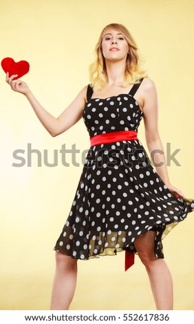 Woman blonde cute girl wearing dotted dress holding red heart love symbol studio shot on bright. Valentines day happiness concept