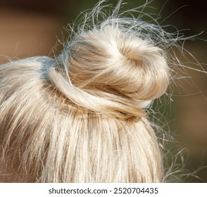 A woman with blonde hair has a bun on her head. The bun is messy and he is a little bit unkempt - Powered by Shutterstock