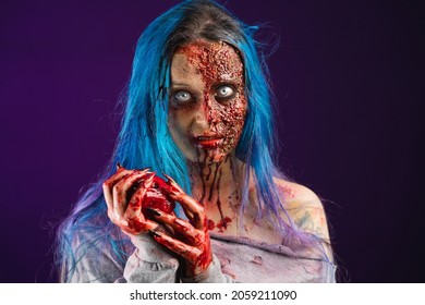 Woman With Bloody Scary Zombie Makeup With White Eyes And Blue Hair Looking At Camera Hands Full Of Blood