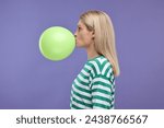 Woman blowing up balloon on violet background