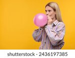 Woman blowing up balloon on yellow background. Space for text