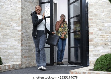 Woman blowing kiss to smiling adult daughter with briefcase leaving apartment building - Powered by Shutterstock