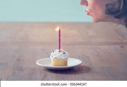 A Woman Blowing Out A Birthday Candle On A Cupcake