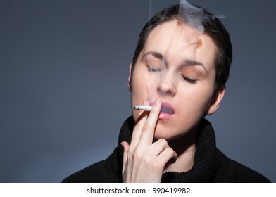 Woman Blowing Smoke Out Of Her Mouth While Smoking Cigarrete On Grey Background