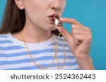 Woman blowing whistle on light blue background, closeup