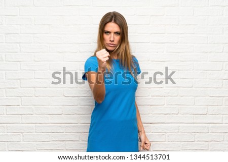 Woman with blue dress over brick wall with angry gesture